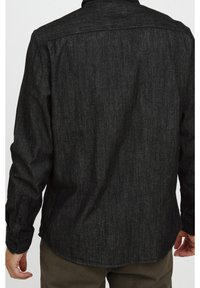 Musta pitkähihaine paita, joka on valmistettu teksturoidusta kankaasta, sisältää nappikaulus, suoraviivainen helma ja klassinen kaulustyyli.