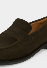 Mocassin en daim marron foncé avec bride penny classique et semelle en caoutchouc noir, montrant des coutures détaillées et une doublure intérieure beige.