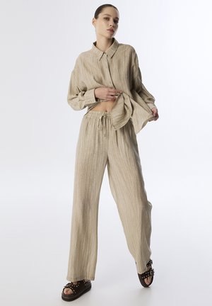 Beige linnen button-up shirt met een kraag, gecombineerd met bijpassende losse broek. Gelaagde stof met subtiele verticale strepen en een elastische tailleband.