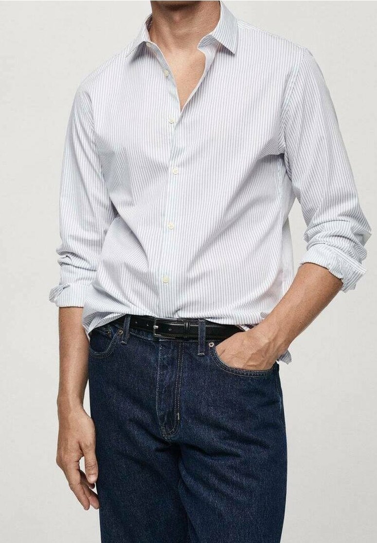 Camisa blanca de cuello con rayas verticales azules, que presenta cierre de botones y mangas arremangadas, combinada con jeans de mezclilla oscura y un cinturón negro.