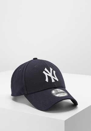 Navy blue baseball cap made of cotton, featuring a white embroidered "NY" logo on the front and an adjustable strap at the back.