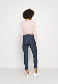 Pantalones de mezclilla azules con un diseño ajustado y bolsillos traseros, combinados con una camiseta de manga larga rosa claro y zapatillas blancas.