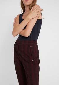 Námořnický tílko spárované s červenými a černými kostkovanými kalhotami. Kalhoty mají boční kapsy a volný střih. Hladká textura látky.