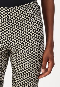 Black pants featuring a cream heart pattern, made from a smooth fabric, with side pockets and a tailored fit.