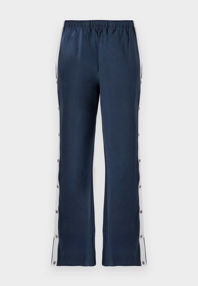 Marineblaue Hose mit strukturiertem Finish, versehen mit einem weißen Seitenstreifen und Druckknöpfen entlang der äußeren Nähte für eine verstellbare Passform.