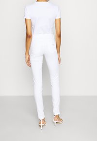 Wit katoenen T-shirt met korte mouwen, gecombineerd met witte skinny jeans. Opvallende details zijn onder andere een klein logo op het achterzakje.