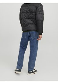 Sort puffervest, grøn strikket foring, blå jeans med lige ben og sorte sneakers med hvide detaljer. Synlige syninger på jeansene.