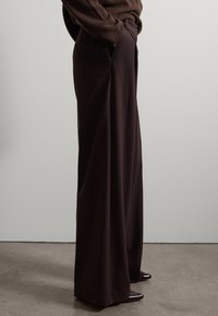 Pantalones marrones de pierna ancha, hechos de una tela suave, con una cintura alta, bolsillos laterales y una textura lisa. Adecuados para un uso informal.
