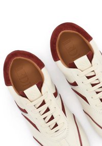 Baskets en cuir blanc avec des détails en daim marron sur les orteils, les côtés et la languette, lacets beige, et logo embossé à l'intérieur de la chaussure.