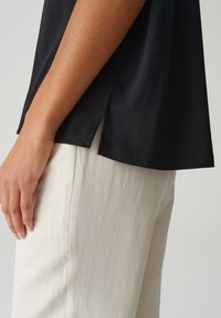 Zwarte T-shirt met een ontspannen pasvorm, zijsplitten en een zachte textuur, gecombineerd met licht beige losse broeken in een gladde stof.