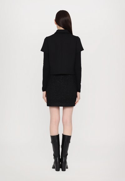 Black cropped jacket with short sleeves and a collar, paired with a black textured mini skirt and knee-high, block-heeled black boots.