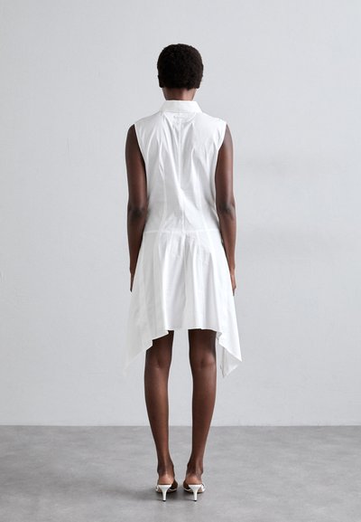 Fehér ujjatlan ruha aszimmetrikus szegéllyel, könnyű anyagból készült, gallérral és hátul gombos részlettel.