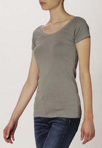 Šedé bavlněné tričko s krátkými rukávy, s výstřihem ve tvaru lodi, ozdobené jemným krajkovým lemem kolem límce. Přiléhavý střih.