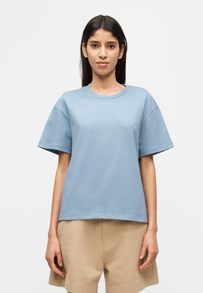 T-shirt en coton bleu à manches courtes, col rond et marquage discret sur le côté gauche. Texture lisse et coupe décontractée.