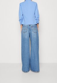 Světle modrá zkrácená bunda s našitými rukávy; doplněná lehkými světle modrými džíny s širokými nohavicemi, které mají dvě zadní kapsy a jemné švy.