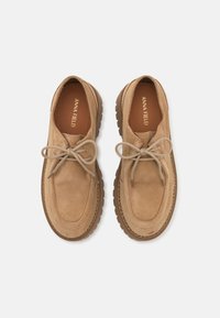 Beige suede lace-up shoes with a rounded toe, rubber sole, and decorative stitching. Features a simple lace design and textured accents.