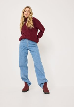 Pull en tricot bordeaux avec un motif chevron texturé, associé à un jean large bleu clair et des bottines bordeaux.