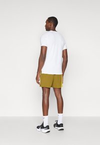 Λευκό κοντομάνικο μπλουζάκι ταιριασμένο με ελαιόχρωμα αθλητικά σορτς που διαθέτουν ανοιχτά πλευρικά αξεσουάρ. Φοριέται με λευκές κάλτσες και μαύρα αθλητικά παπούτσια.