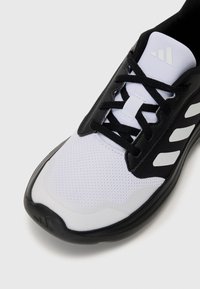 Baskets noires et blanches avec une tige en maille, bout rond, lacets noirs et trois rayures noires sur le côté ; semelle en caoutchouc texturée.