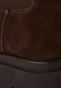 Brauner Velourslederschuhabschnitt mit einer glatten schwarzen Sohle, sichtbaren Nähten und einem abgerundeten Zehendesign.