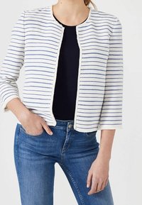 Valkoraidallinen takki, jossa siniset viivat, avoin etuosa ja kolme neljäsosan hihat, päällä mustan yläosan kanssa, yhdistetty sinisiin farkkuihin.