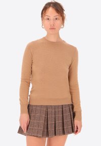 Maglione di cotone marrone chiaro con maniche lunghe e scollo rotondo, abbinato a una gonna plissettata a quadri marrone con linee sottili.