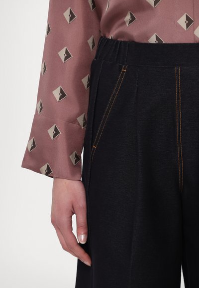 Ruskea kuvioitu paita, jossa on geometrisia muotoja, yhdistetty tummansinisille housuille, joissa on oranssia ommelta ja laskostettu etuosa.