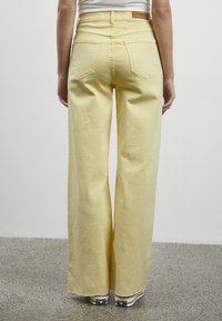 Pantaloni larghi a vita alta gialli in denim, con due tasche posteriori e un'etichetta in pelle beige sul punto vita.