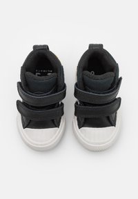 Zapatillas para niños en negro y gris, con dos correas de Velcro, puntera de goma blanca, suela texturizada y interior acolchado para mayor comodidad.