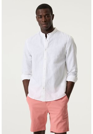 Weißes Leinenhemd mit Knöpfen und Stehkragen, lange aufgerollte Ärmel, kombiniert mit hellrosa Shorts. Einfaches und lässiges Design.