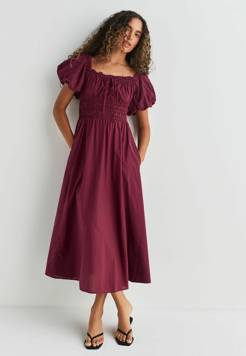 Bordeaux maxi klänning med puffärmar, smockad bodice och sidofickor, tillverkad av lättviktig tyg, med fyrkantig halsringning.