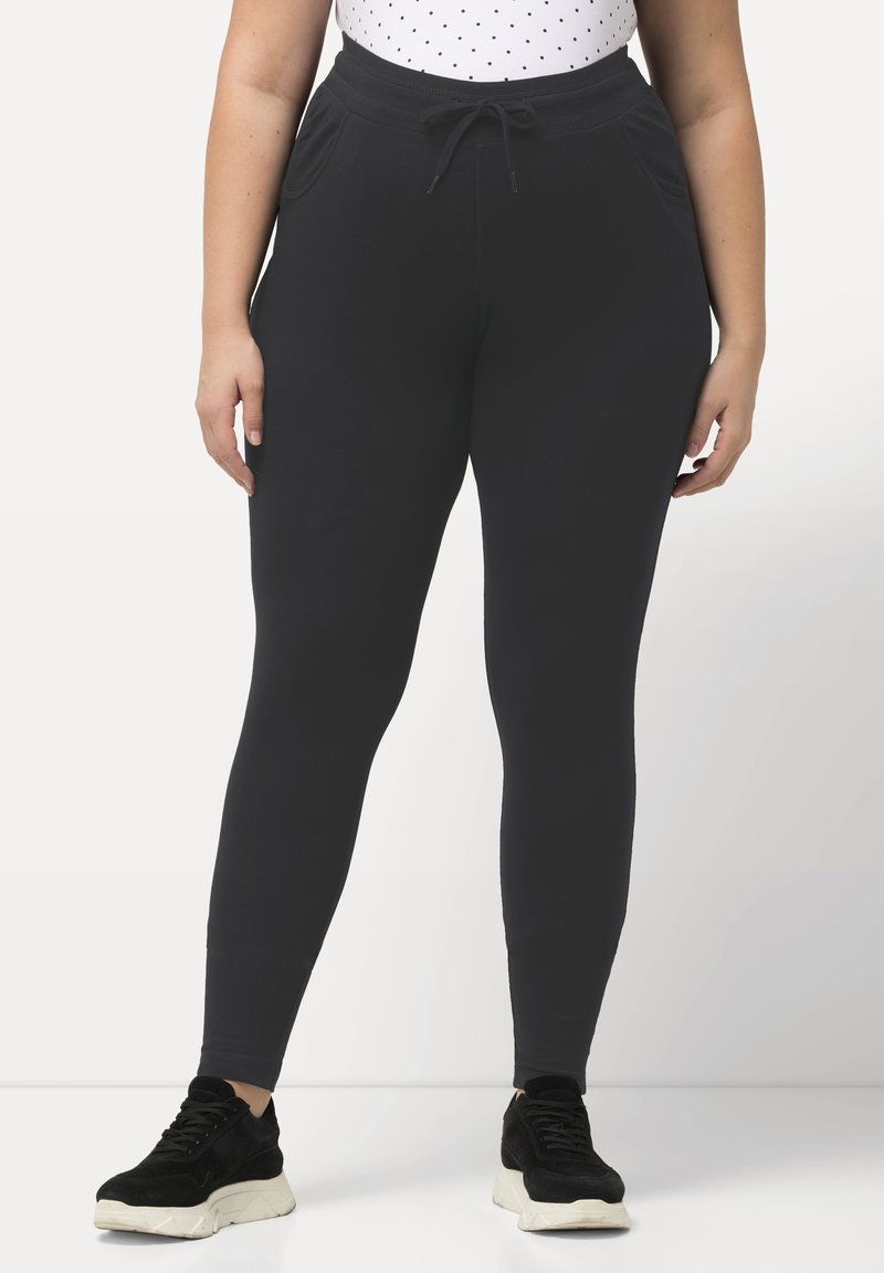 Schwarze Leggings aus Polyester-Mix mit passgenauer Passform, elastischem Bund, Kordelzug und Taschen an den Seiten, kombiniert mit dunklen Sneakers.