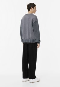 Szary sweter z teksturowymi rękawami, prążkowanym dołem i oversize'owym krojem, zestawiony z szerokimi czarnymi spodniami i białymi trampkami.
