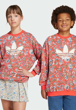Bloemrijke sweatshirts in rood en groen met een witte Adidas-logo, ronde hals en lange mouwen. Model draagt een rok met bloemenprint.