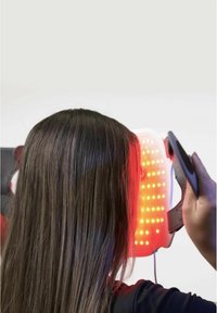 Dispositif de thérapie par lumière LED ; présentant un panneau blanc avec des lumières rouges, des sangles ajustables et un design élégant utilisé près de la tête d'une personne.