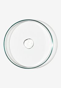 Piastra di Petri in vetro trasparente con bordo rialzato, posata su una superficie bianca, contenente una piccola goccia di liquido trasparente al centro.