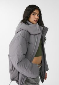 Graue Daunenjacke mit hohem Kragen, Reißverschluss und Druckknöpfen. Verfügt über eine voluminöse Silhouette und elastische Bündchen für zusätzliche Wärme.