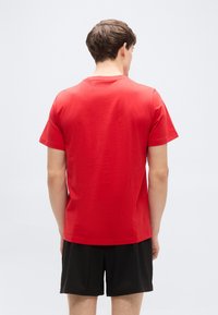 Κόκκινο κοντομ άνικο μπλουζάκι από βαμβάκι, με απλό σχέδιο, στρογγυλή λαιμόκοψη και λείο ύφασμα. Φοριέται με μαύρο σορτς.