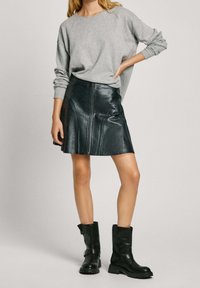 Sweat-shirt gris à manches longues, jupe trapèze en cuir noir avec fermeture éclair frontale, et bottines noires. Textures lisses avec accents minimalistes.