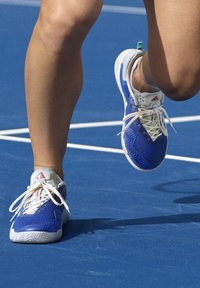 Scarpe da ginnastica blu con accenti e lacci bianchi, dotate di una suola testurizzata e un logo discreto sul lato, posizionate su una superficie di campo blu.