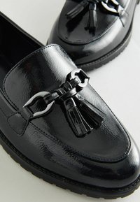Schwarze Lackleder-Loafer mit abgerundetem Zehenbereich, dekorativem Quastenakzent und silberner Schnalle. Die Gummisohle sorgt für Halt.