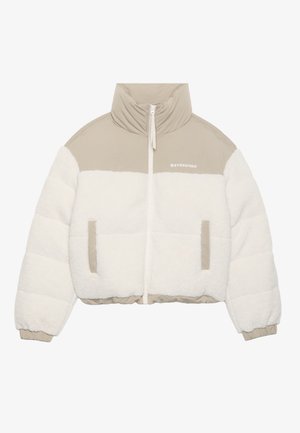 Lyhennetty takki, jossa on beige yläosa ja valkoinen pörröinen fleece-alareuna. Varustettu etuvetoketjulla, kahdella sivutaskulla ja korkealla kauluksella.