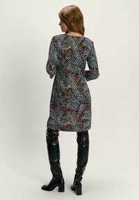 Gemustertes Kleid mit langen Ärmeln, das eine Mischung aus Blau, Rot und Schwarz zeigt; getragen mit glänzenden schwarzen Overkneestiefeln.