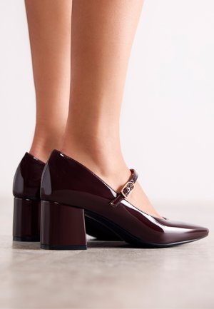 Chaussures à talons en cuir laqué bourgogne avec un bout arrondi et une fine sangle à la cheville avec une boucle argentée, design de talon bloc surélevé.