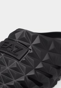 Κοντινό πλάνο μαύρου σαγιοναριού EA7 με γεωμετρική υφή και ανάγλυφο λογότυπο της μάρκας στο λουράκι.