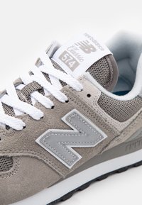 Šedé tenisky New Balance Classic 574 s bílými tkaničkami, svršek z mezipaměti a semiše, polstrovaný límec, s logem na boku a štítkem na jazyku.