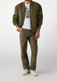 Olijfgroene bomberjack met bloemenborduursel, wit graphic t-shirt, olijfgroene cargobroek en witte sneakers. Casual fit.
