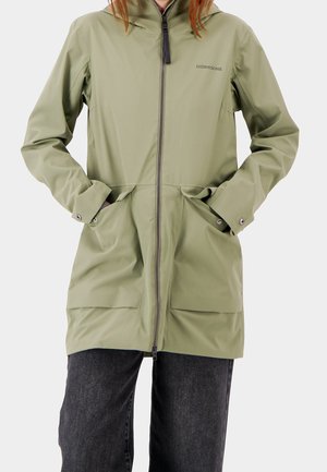 Persona con chubasquero con capucha de cremallera en verde claro, con bolsillos laterales y broches en los puños, combinado con pantalones gris oscuro.