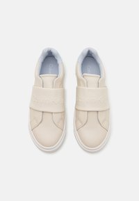 Calvin Klein beige slip-on sko med en teksturert læroverdel, som har et bredt belte med preget logo, lyseblå innersåle og hvit såle.