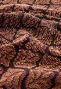 Texturovaná látka tmavě černé barvy s růžovými a zlatými listovými vzory. Povrch působí bohatým a prostorovým dojmem a ukazuje složitý vzor tkaní.